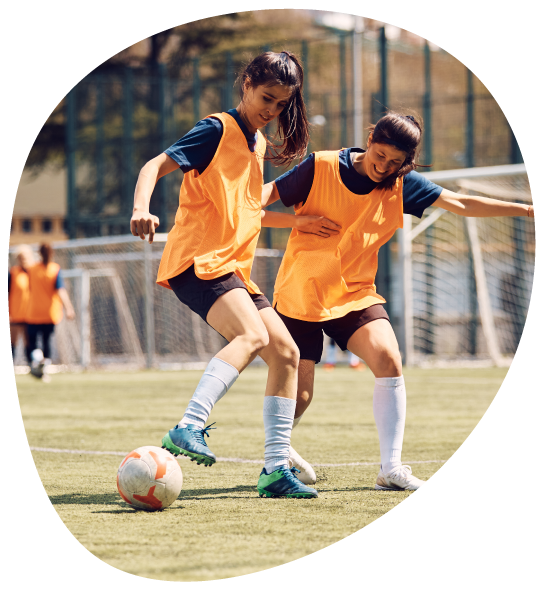 Two high school girls playing soccer on a soccer field.