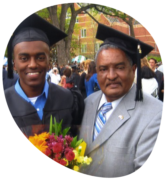 A high school graduate with his father, both wearing graduation caps.